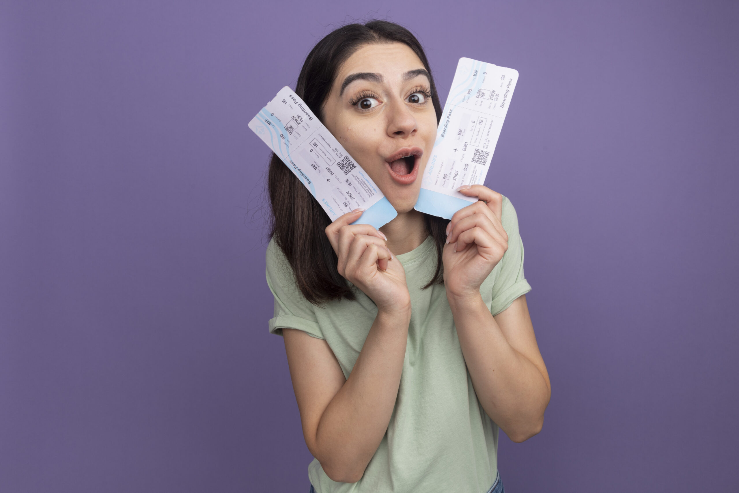 impressed young pretty caucasian girl looking at camera holding airplane tickets touching face with them looking at camera isolated on purple background with copy space