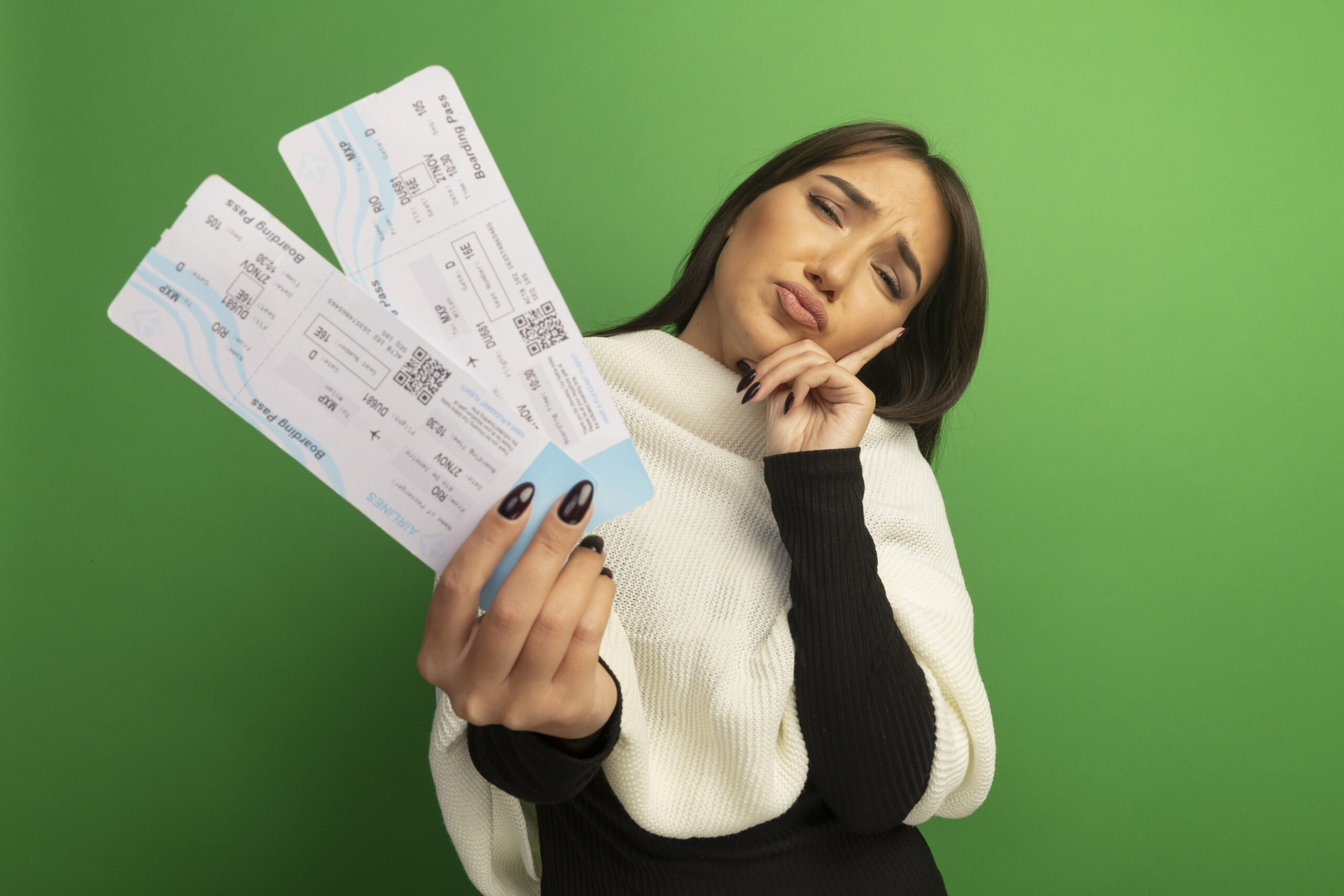 young woman with white scarf showing air tickets looking at camera confused and very anxious standing over green background